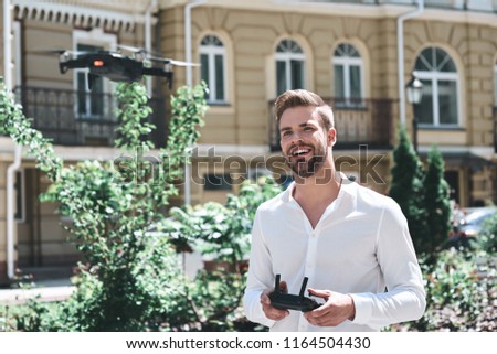 Young man control drone while sitting at pier in old european city