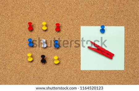 Nine color buttons and a sticker with a clothespin on a cork board
