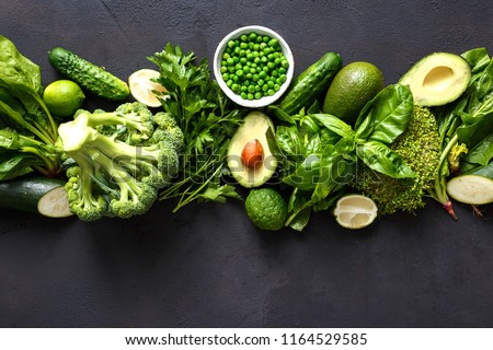 Raw healthy food clean eating vegetables: cucumber, alfalfa, zucchini, spinach, basil, green peas, dill, parsley, avocado, broccoli, lime on dark stone background, top view Royalty-Free Stock Photo #1164529585