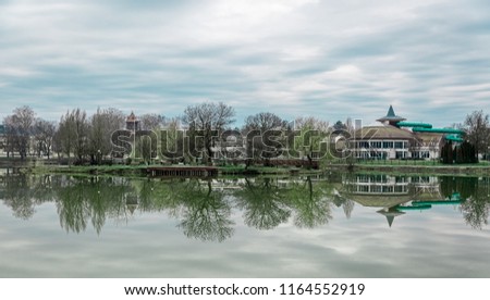 Beautiful lake with mirror reflections in clear water on cloudy day. Tranquil landscape with lake, trees and cloudy sky. Nyiregyhaza, Hungary. Toned photo