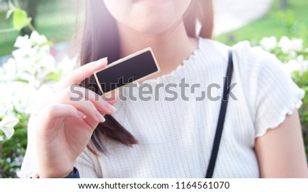 Image of White shirt woman show close-up blank black card by right hand. Flare background.