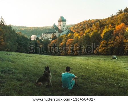 A man in a park with a dog with a stunning view of the underwater sunset, Karlstejn gothic castle near Prague, the most famous castle in Czech Republic, autumn season