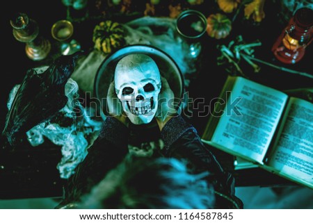 Top view of a magic skull in witch's hands above pot with poison potion.