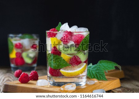 Two glasses of fresh mineral water, with berries and fruits (raspberry, lemon, kiwi, cherry) and ice on a black background. Copy Space