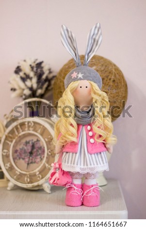 Doll textile handmade bunny in a pink jacket and boots in a scarf on the background of the interior of your room with a handbag