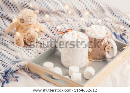 Two cups of hot chocolate with marshmallows on soft plaid background with beautiful Christmas lights and books. Perfect winter time treat. 