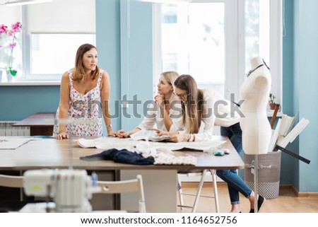 Three smart-looking pretty women are pointing at the sewing magazine. Tailor's dummy is in the background. Fashion, tailor's workshop.