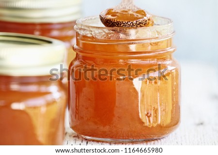 Wooden spoon full of homemade Cantaloupe Jam resting in an open jar filled with jam. Shallow depth of field with selective focus on mason jar in center. Image could be used for peach jam or marmalade.