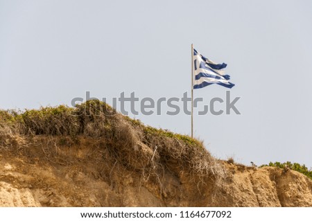 Flag of greece in the wind on the rock with nice blue sky in background