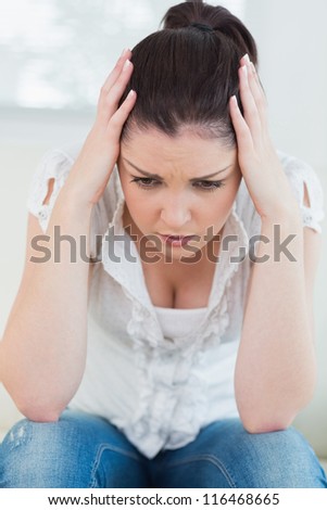 Unnerved woman sitting on a couch and holding her hands at her head Royalty-Free Stock Photo #116468665