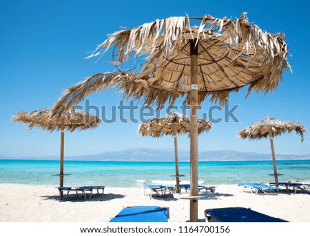 Two Deckchairs Under Parasol In Tropical Beach at quiet sea