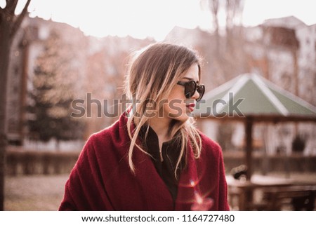 modern young woman in black coat with sunglasses and red scarf. relaxed park scene
