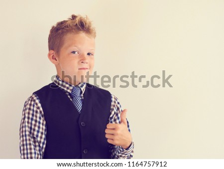Smiling little schoolboy showing thumb up standing near the white blackboard.