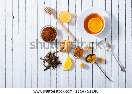 cup of tea, different leaves, honey, lemon ginger and brown sugar on white wooden table background