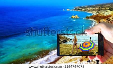 Vibrant image of blue emerald sea near the birthplace of Aphrodite with human hand and smart phone dispaying bikini girls