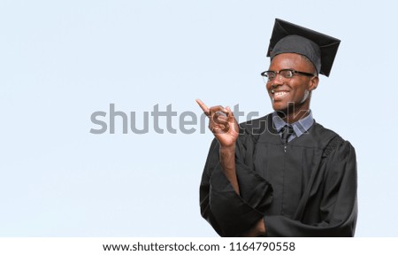 Young graduated african american man over isolated background with a big smile on face, pointing with hand and finger to the side looking at the camera.