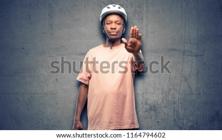 Black man wearing bike helmet annoyed with bad attitude making stop sign with hand, saying no, expressing security, defense or restriction, maybe pushing