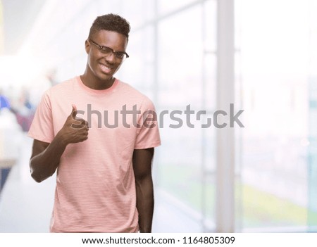 Young african american man wearing pink t-shirt doing happy thumbs up gesture with hand. Approving expression looking at the camera with showing success.
