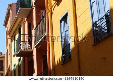 Outdoor view of a typical street of Collioure village, southern France. August, 26, 2018. Colorful facades with wooden doors and windows, and small iron balconies. Sunny day, blue sky in background.