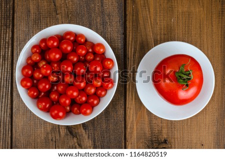 Small red cherry tomatoes in white bowl on wooden background. Studio Photo