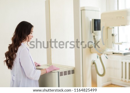 The young happy breast specialist standing near the apparatus of the ultrasound examination of the breast in her office