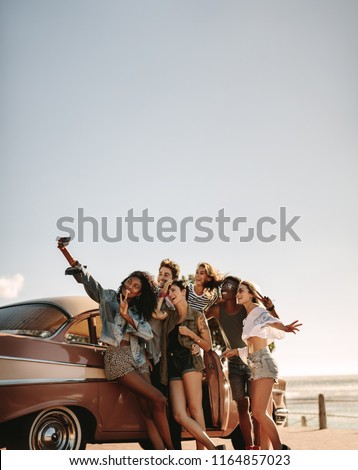 Group of multi ethnic people taking a selfie near the car. Young men and women together on road trip making selfie.