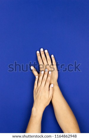A young beautiful girl showing her tender hands with nice white or pastel pink manicured nails on a blue background in a beauty salon. Flat lay photo.