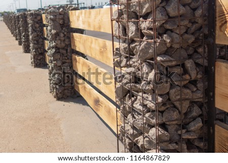 Wooden fence made of horizontal boards with stone pillars. The pillars are made of a metal frame with granite gravel embedded in it. Option of decorative use of gravel.