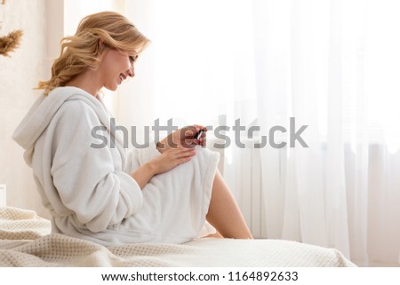 Shapely woman painted her nails in the morning, while sitting on the bed being dressed in a dressing-gown.