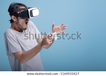 Young bearded man playing VR game in blue background. Shocked Asian young hipster wearing VR headset, half body shot. Young generation hipster relaxation concept.
