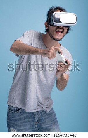 Young bearded man playing VR game in blue background. Very excited Asian young hipster wearing VR headset, half body shot. Young generation hipster relaxation concept.