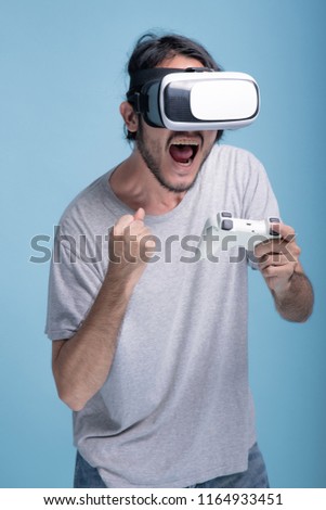 Young bearded man playing VR game in blue background. Extreamly excited Asian young hipster wearing VR headset, half body shot. Young generation hipster relaxation concept.