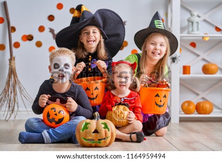 Happy brother and three sisters on Halloween. Funny kids in carnival costumes indoors. Cheerful children play with pumpkins and candy.