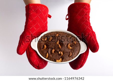 Woman wearing red gloves protect her hands holding chocolate brownie in ceramic baking tray  on white table background Royalty-Free Stock Photo #1164976342