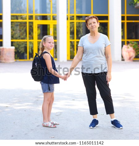 Grandma and pupil kid holding hands going to school.Little girl with school bag or satchel walking to school with grandmother. Old Parent and daughter, grandmother and granddaughter, back to school. 
