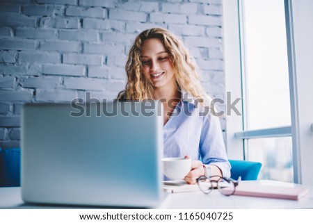 Happy woman watching positive videos via media app on laptop computer with good internet, cheerful hipster girl resting in coffee shop creating publication for content web page via modern netbook