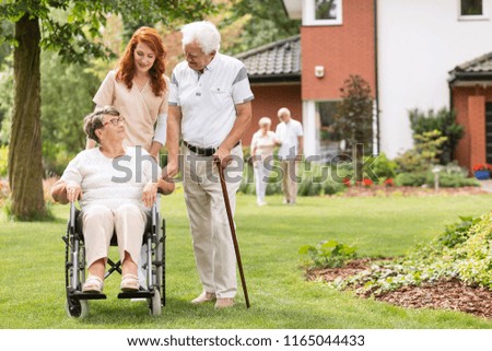 An elderly disabled couple with their caretaker in the garden outside of a private rehabilitation clinic. Royalty-Free Stock Photo #1165044433