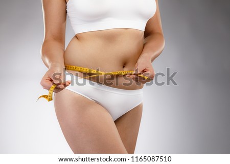Woman measuring waist on gray background 