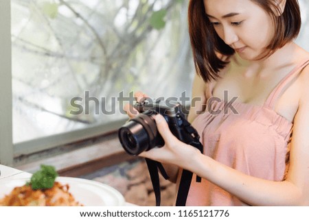 Close up of a asian blogger woman  taking photos of food using a professional camera for her food blog. Thai female food blogger shooting photos for her blog on table at resturant.