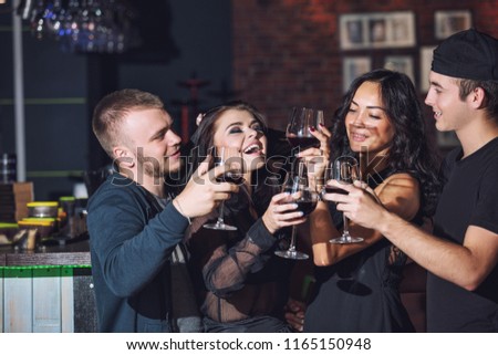 Company of beautiful young happy friends in the bar with glasses of wine to celebrate