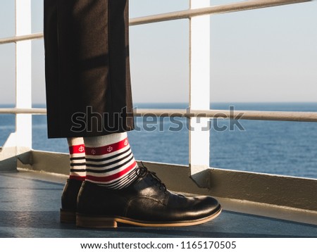 Men's legs in stylish, black shoes, dark pants and funny, bright, striped socks with a pattern on the deck of a cruise ship. Concept of lifestyle, fashion and fun