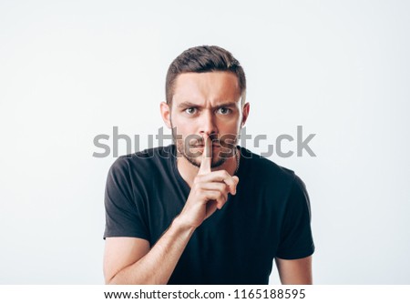 Young man holding index finger on lips asking for silence.  Secret concept
