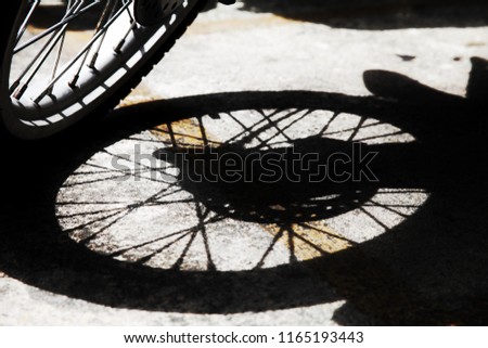 shadow of single motorbike wheel spoke and rim from sunlight parking on concrete road and yellow line background, closed up, black and white artwork concept