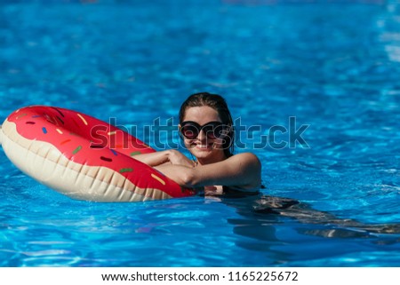 Beautiful young woman with pink donut circle have rest  in blue swimming pool