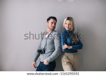 Photo of a handsome man with a camera and a pretty woman standing by the grey wall