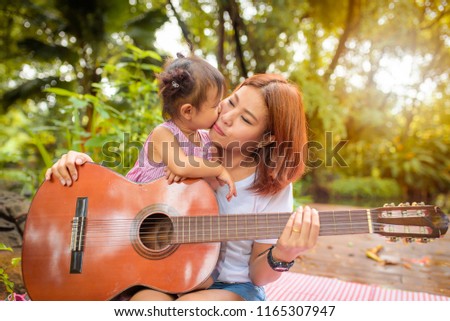 Girl with mother playing guitar in garden and the daughter kisses her mother's cheek.Mother's Day, mother's love, mother and child love