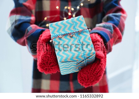 Person in mittens holding Christmas gift box, closeup