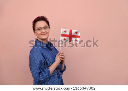 Georgia flag. Woman holding Georgia flag. Nice portrait of middle aged lady 40 50 years old with a national flag over pink wall background outdoors.