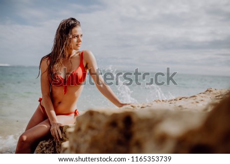 Freedom Young woman in red bikini sitting on the cliff near Sea Alone.