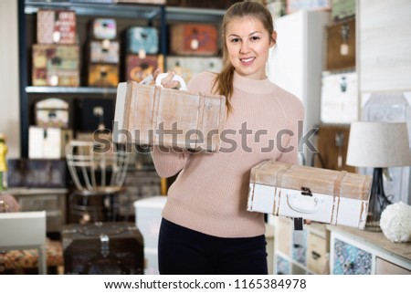 Smiling  cheerful happy positive  woman buyer holding wooden suitcase in furniture shopping room 